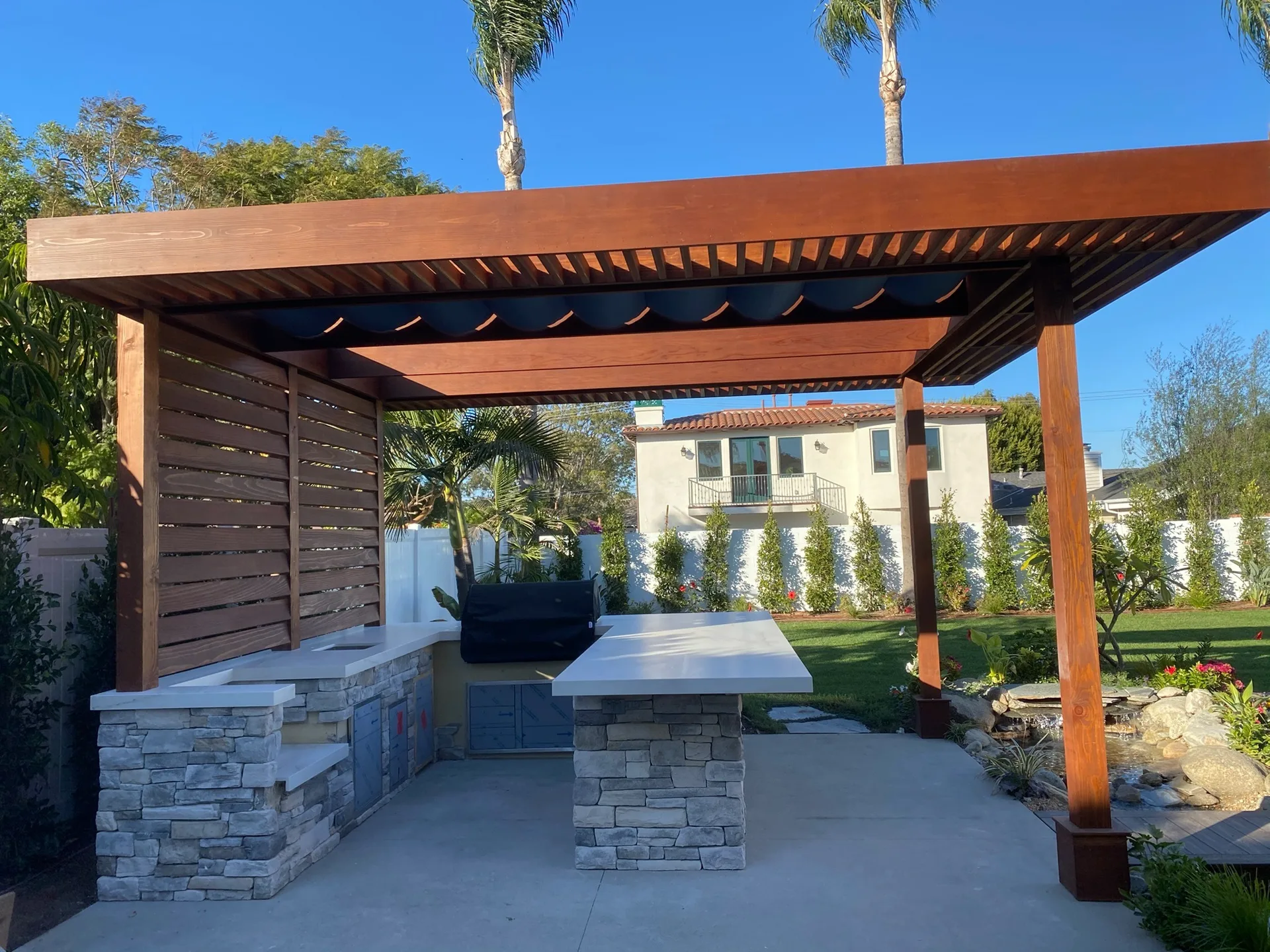 Outdoor kitchen with stone island under a pergola on a finished patio