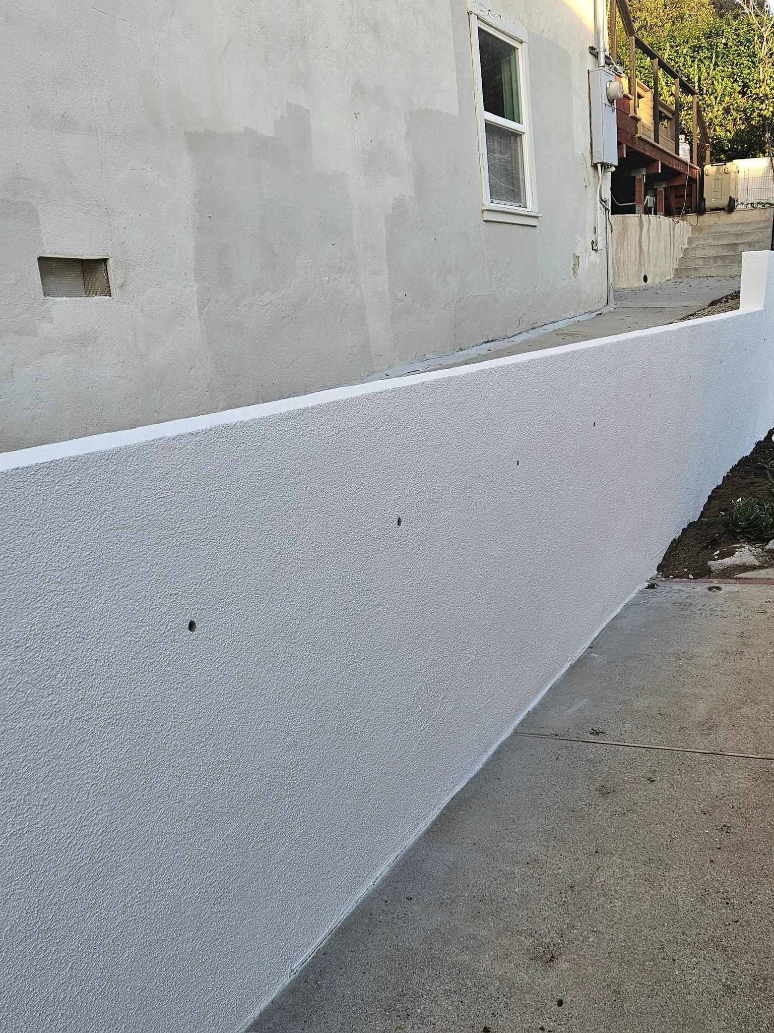 Repaired wall refinished in white stucco beside a walkway